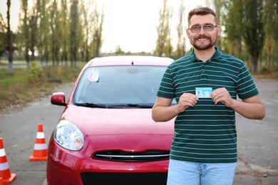Happy man showing driving license near new car outdoors