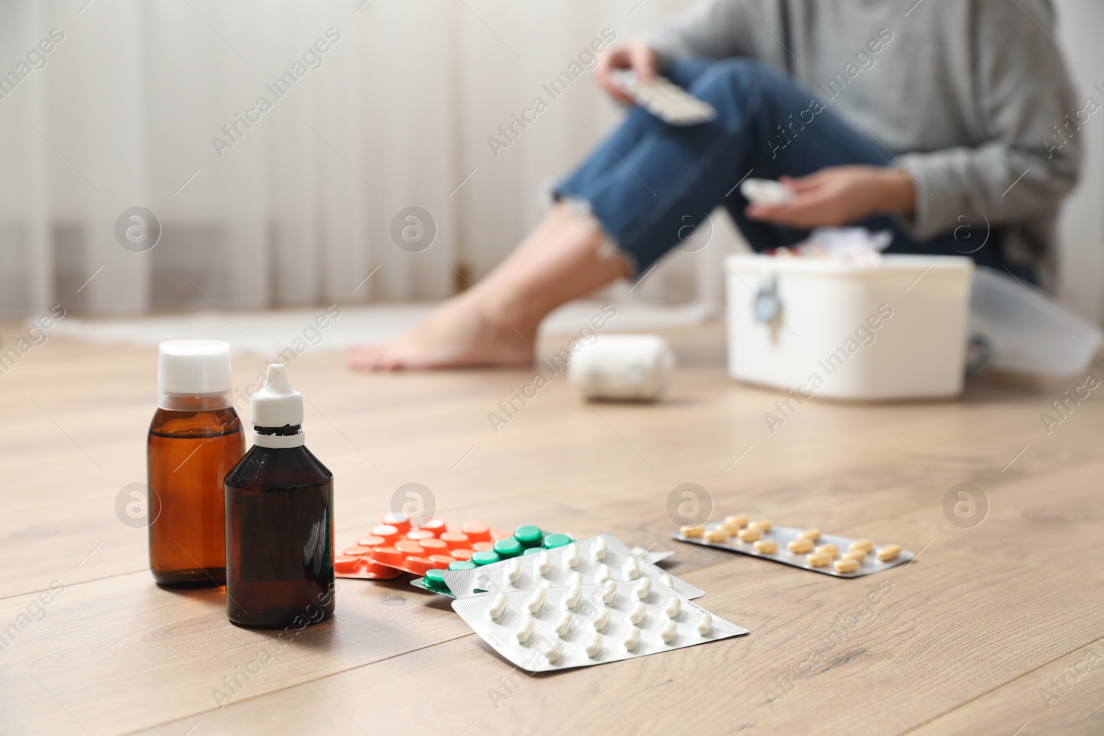 Photo of Woman with first aid kit sitting on floor indoors, focus on medicaments