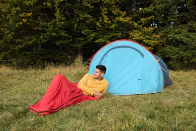 Man in sleeping bag near camping tent outdoors