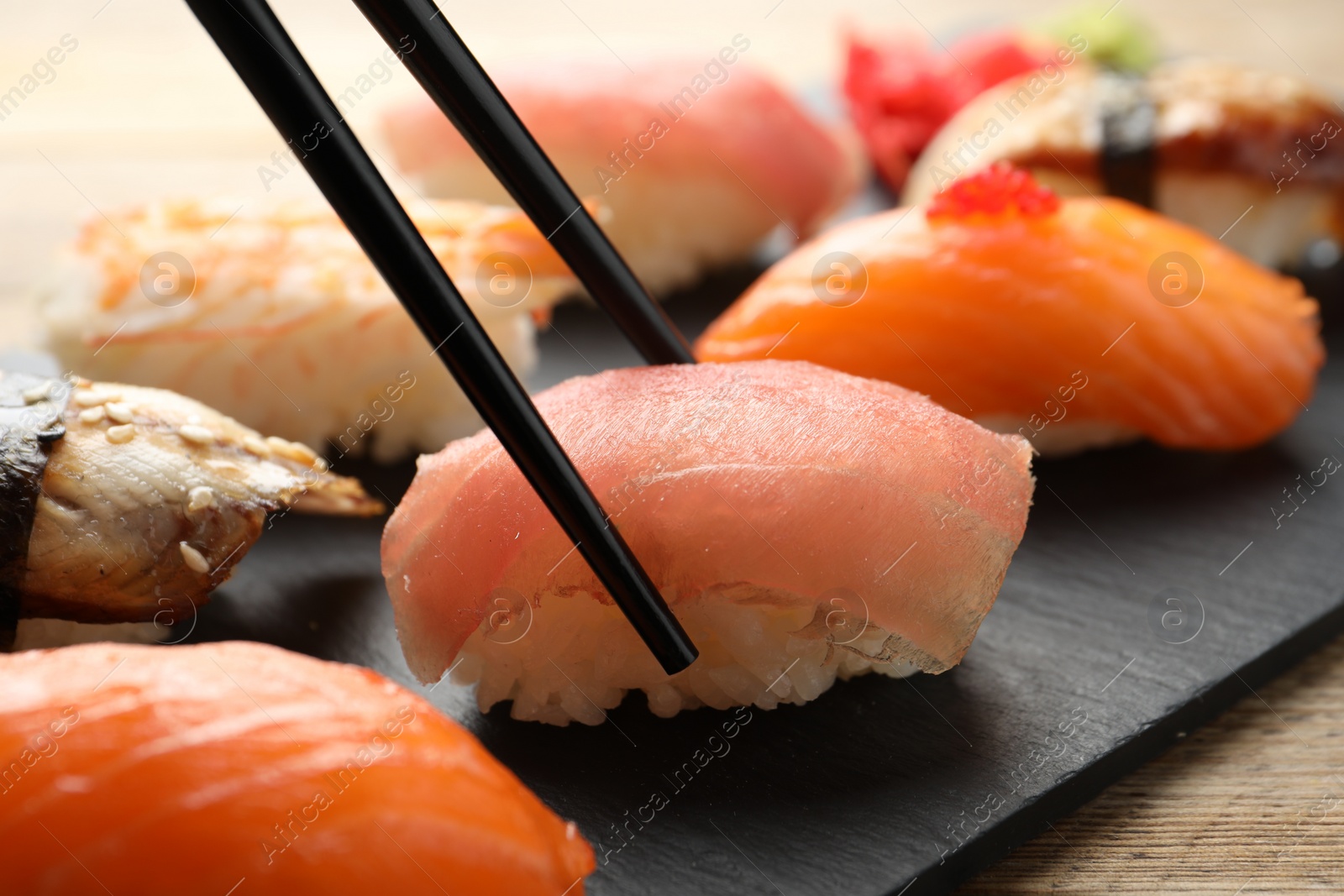 Photo of Taking delicious nigiri sushi with chopsticks on wooden table, closeup