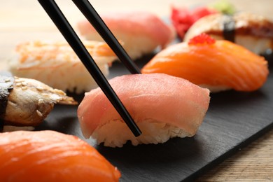 Photo of Taking delicious nigiri sushi with chopsticks on wooden table, closeup
