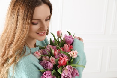 Photo of Young woman with bouquet of beautiful tulips indoors. Space for text
