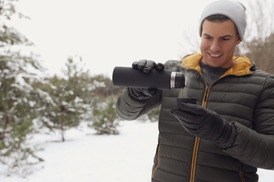 Photo of Man pouring hot drink from thermos into cap outdoors on snow day