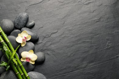 Photo of Spa stones, beautiful orchid flowers and bamboo stems on black table, flat lay. Space for text