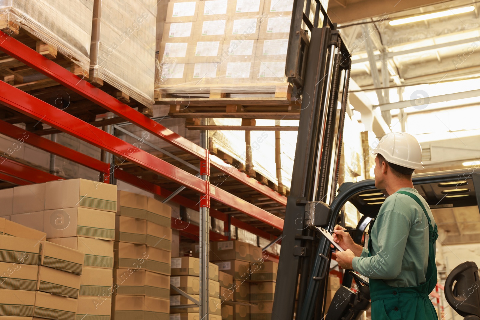 Image of Worker near forklift truck with cardboard boxes in warehouse. Logistics concept