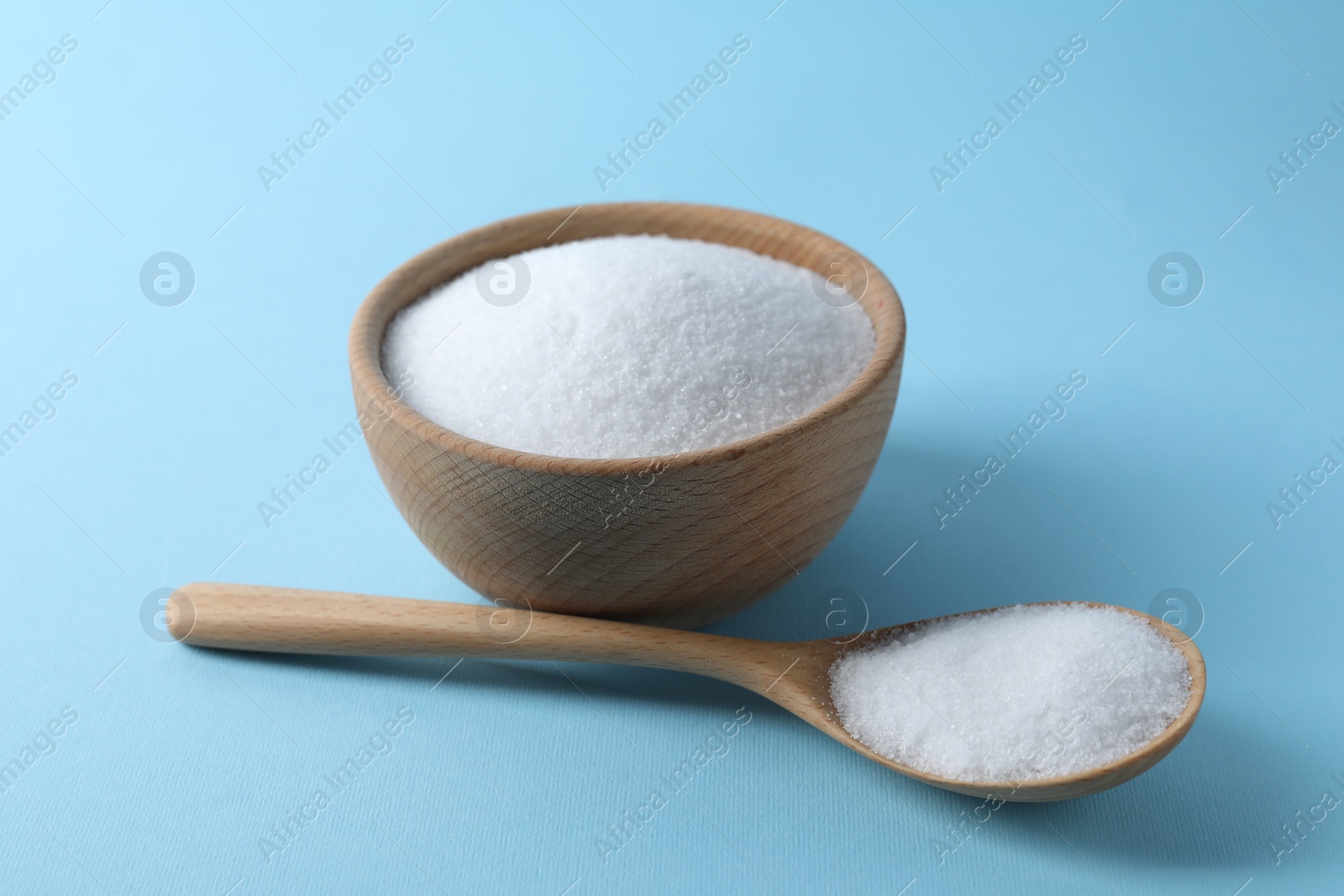 Photo of Organic white salt in bowl and spoon on light blue background