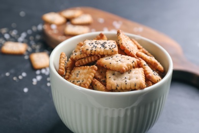 Photo of Delicious crispy crackers in bowl on black table, closeup