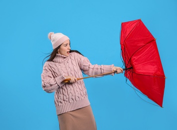 Photo of Young woman with umbrella caught in gust of wind on light blue background