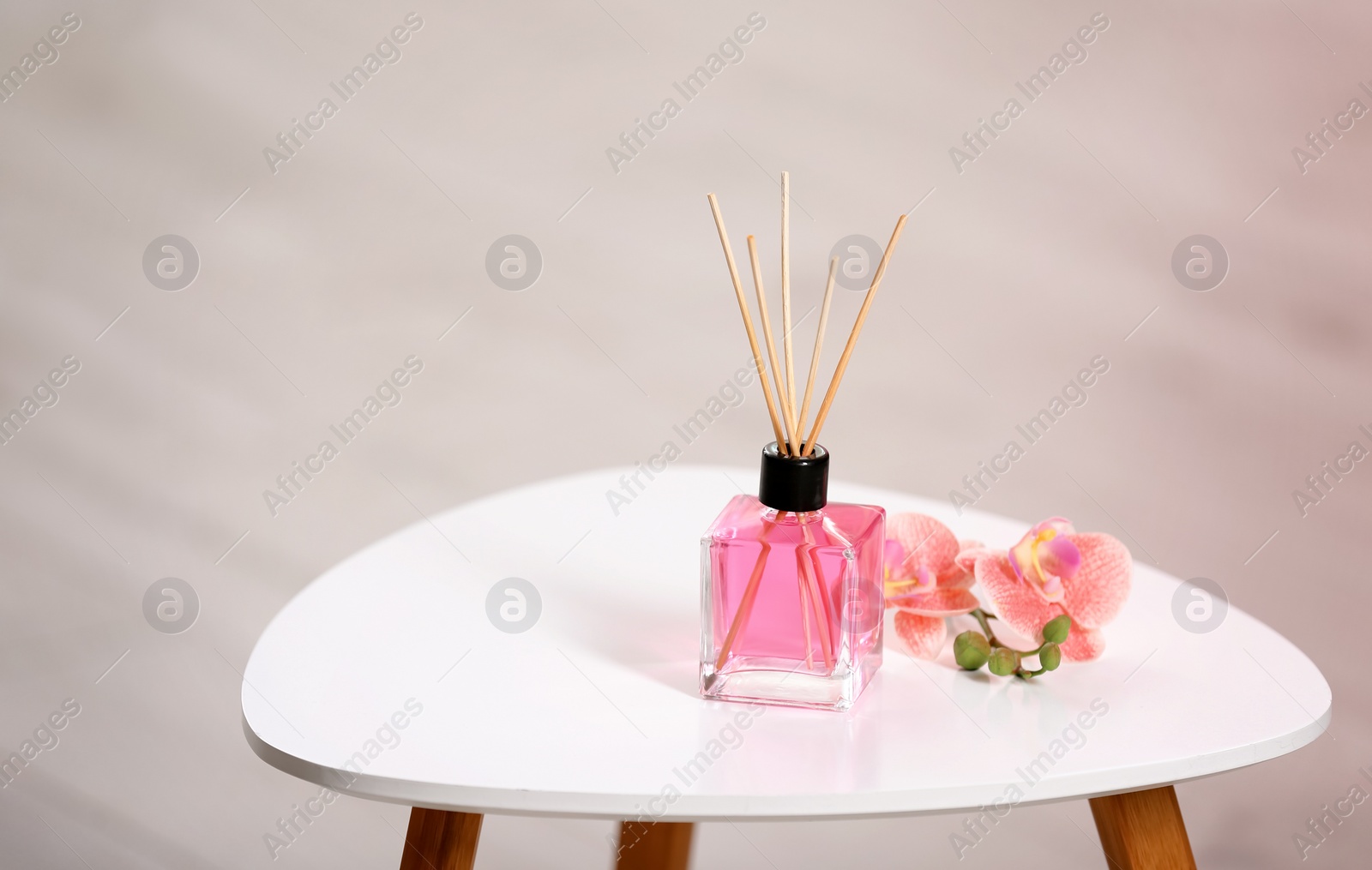 Photo of Aromatic reed air freshener and flowers on table against blurred background