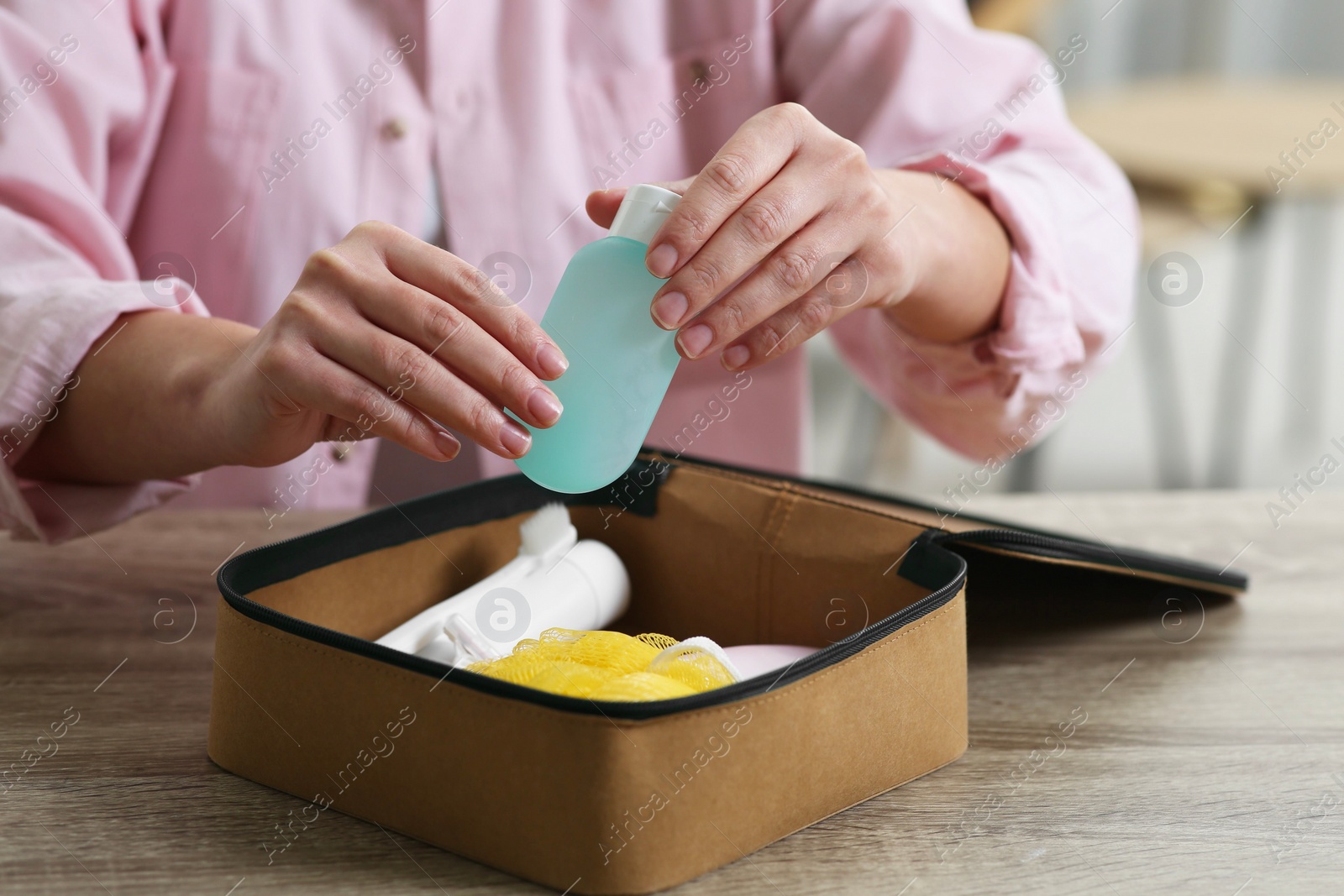 Photo of Woman packing cosmetic travel kit into compact toiletry bag at wooden table indoors, closeup. Bath accessories