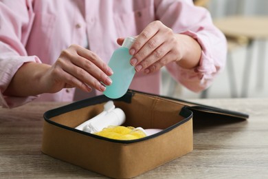 Photo of Woman packing cosmetic travel kit into compact toiletry bag at wooden table indoors, closeup. Bath accessories