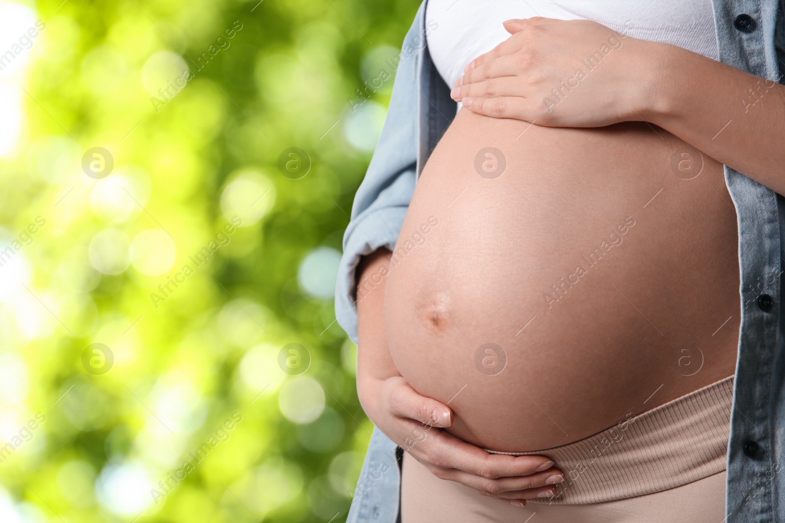 Image of Young pregnant woman touching her belly outdoors, closeup. Space for text