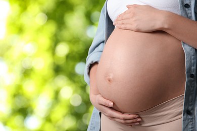 Young pregnant woman touching her belly outdoors, closeup. Space for text