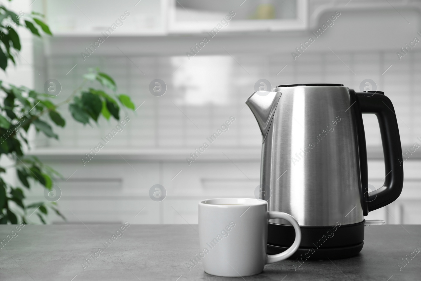 Photo of Modern electric kettle and cup on grey table in kitchen. Space for text