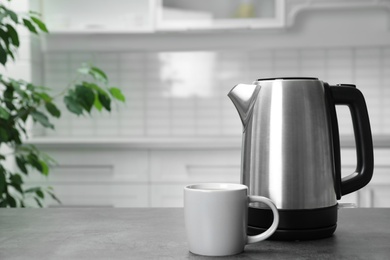 Photo of Modern electric kettle and cup on grey table in kitchen. Space for text