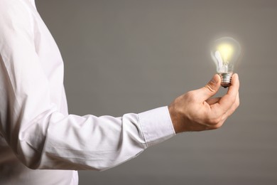 Photo of Glow up your ideas. Closeup view of man holding light bulb on grey background