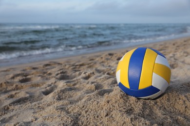 Photo of Colorful volleyball ball on sand near sea. Space for text
