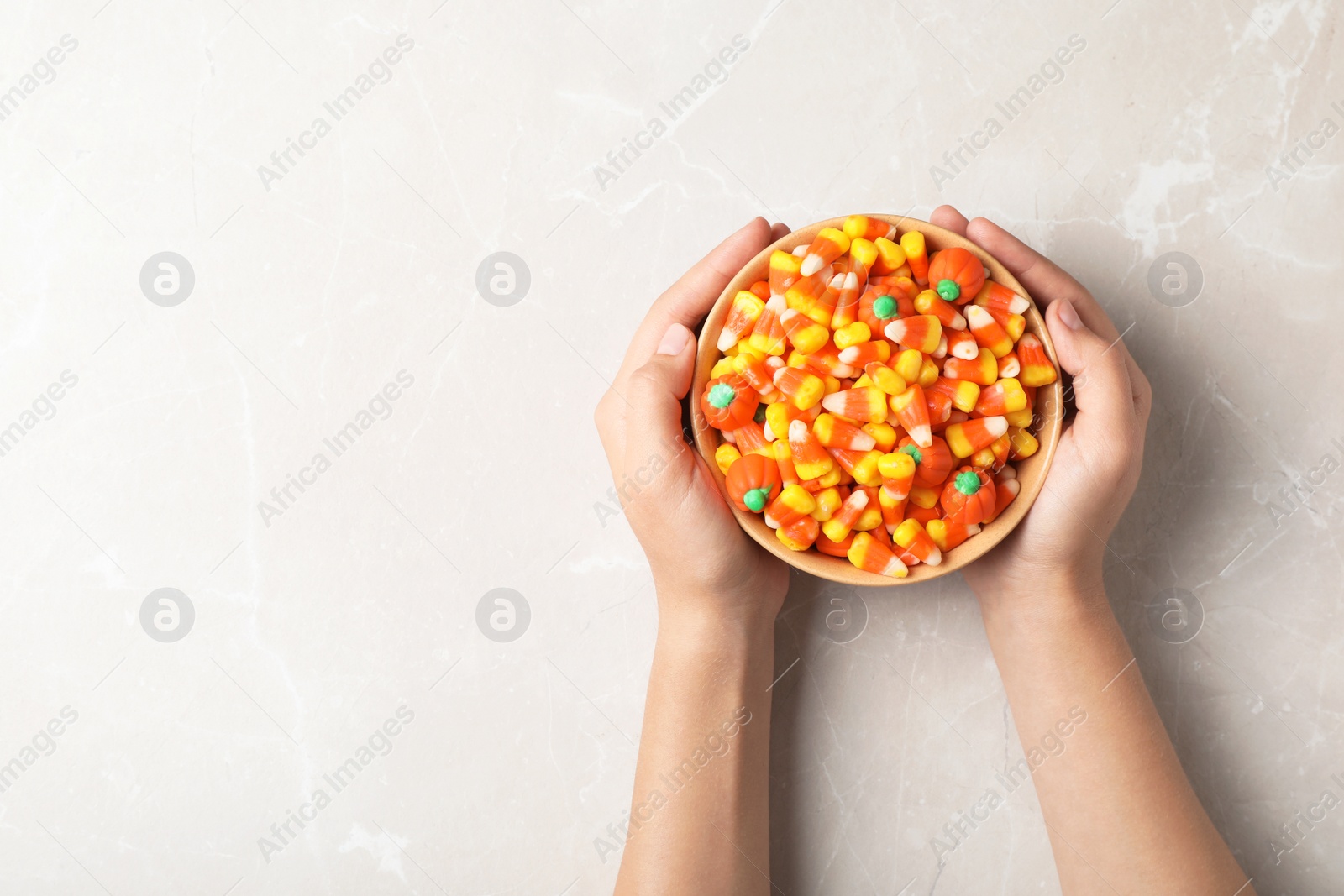 Photo of Woman holding bowl of delicious candies on gray background, top view. Space for text