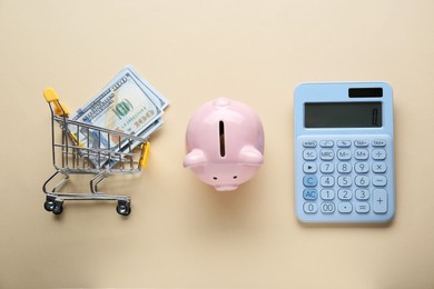 Photo of Calculator, piggy bank and cart with money on beige background, flat lay