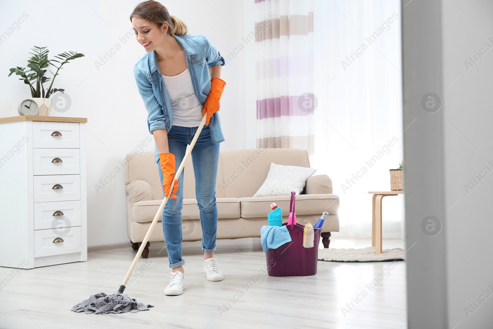 Photo of Young woman washing floor with mop in living room. Cleaning service