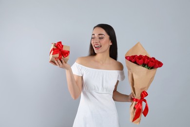 Photo of Happy woman with red tulip bouquet and gift box on light grey background. 8th of March celebration