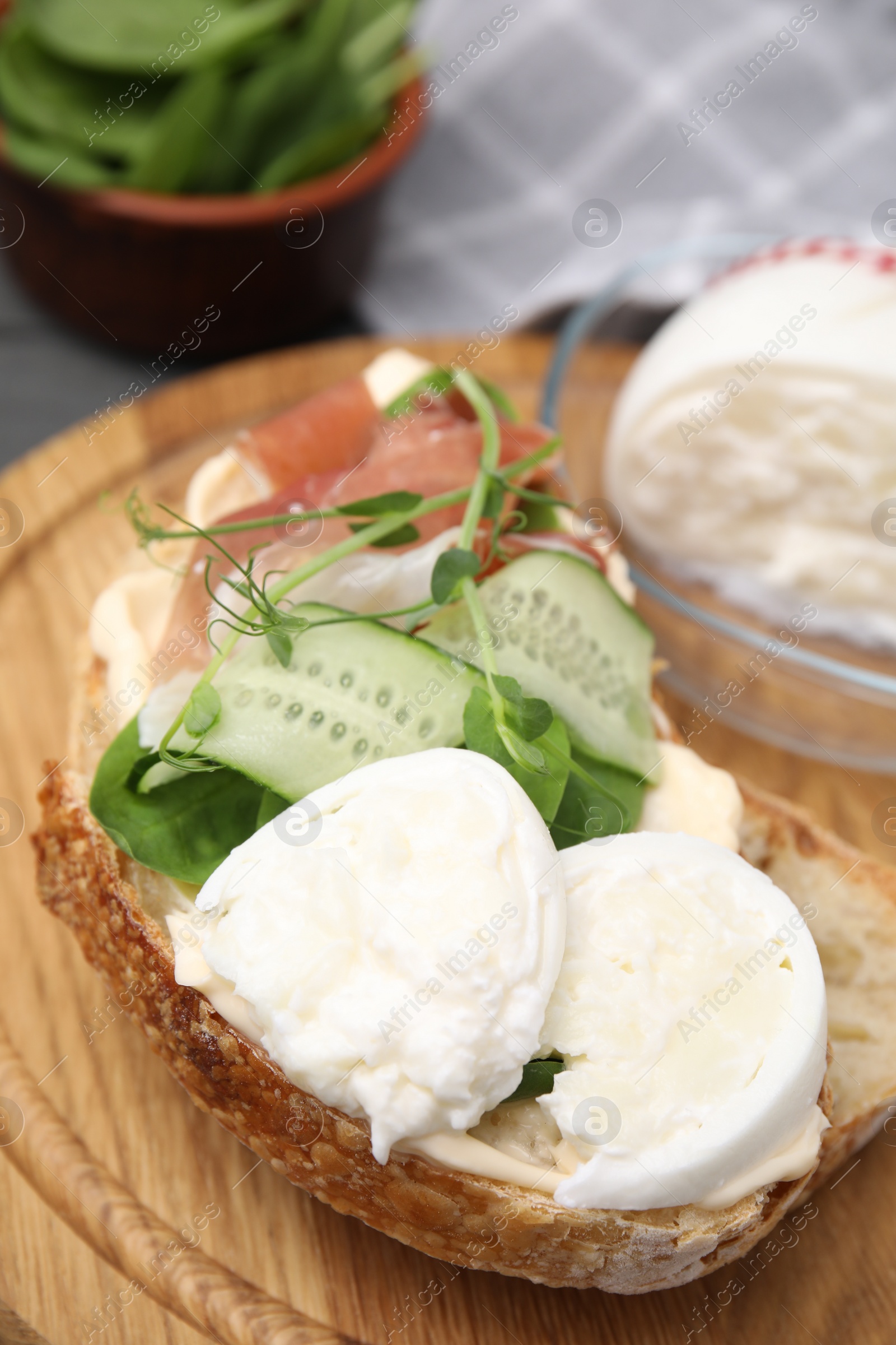 Photo of Tasty sandwich with burrata cheese, prosciutto and cucumber on wooden board, closeup