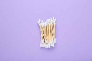 Wooden cotton buds on violet background, flat lay