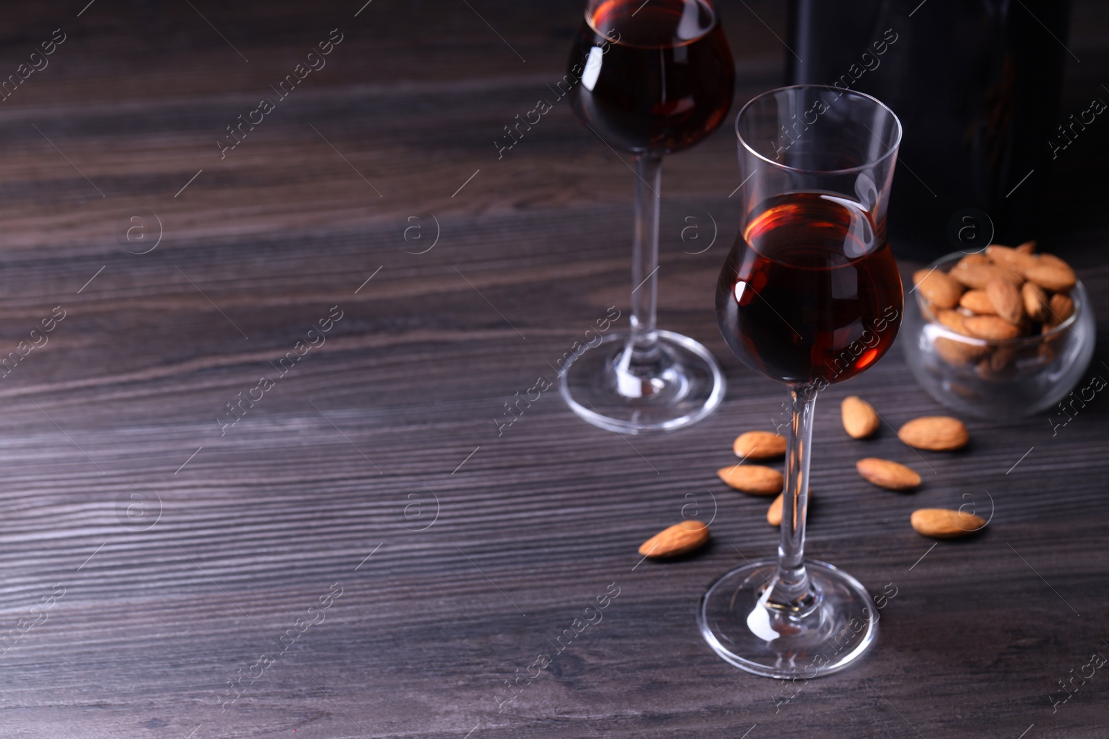 Photo of Liqueur glasses with tasty amaretto and almonds on wooden table, space for text