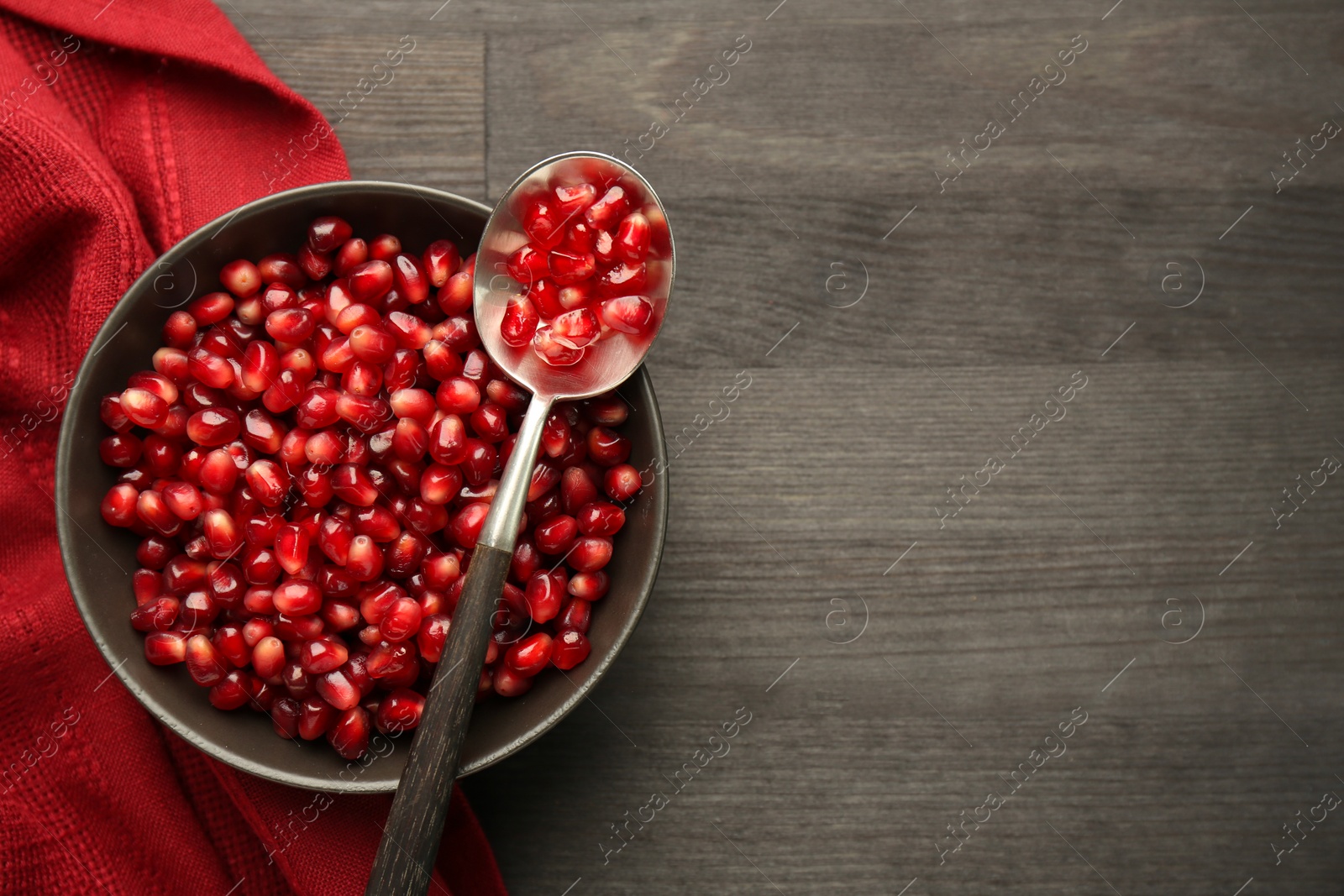 Photo of Tasty ripe pomegranate grains on dark wooden table, top view. Space for text