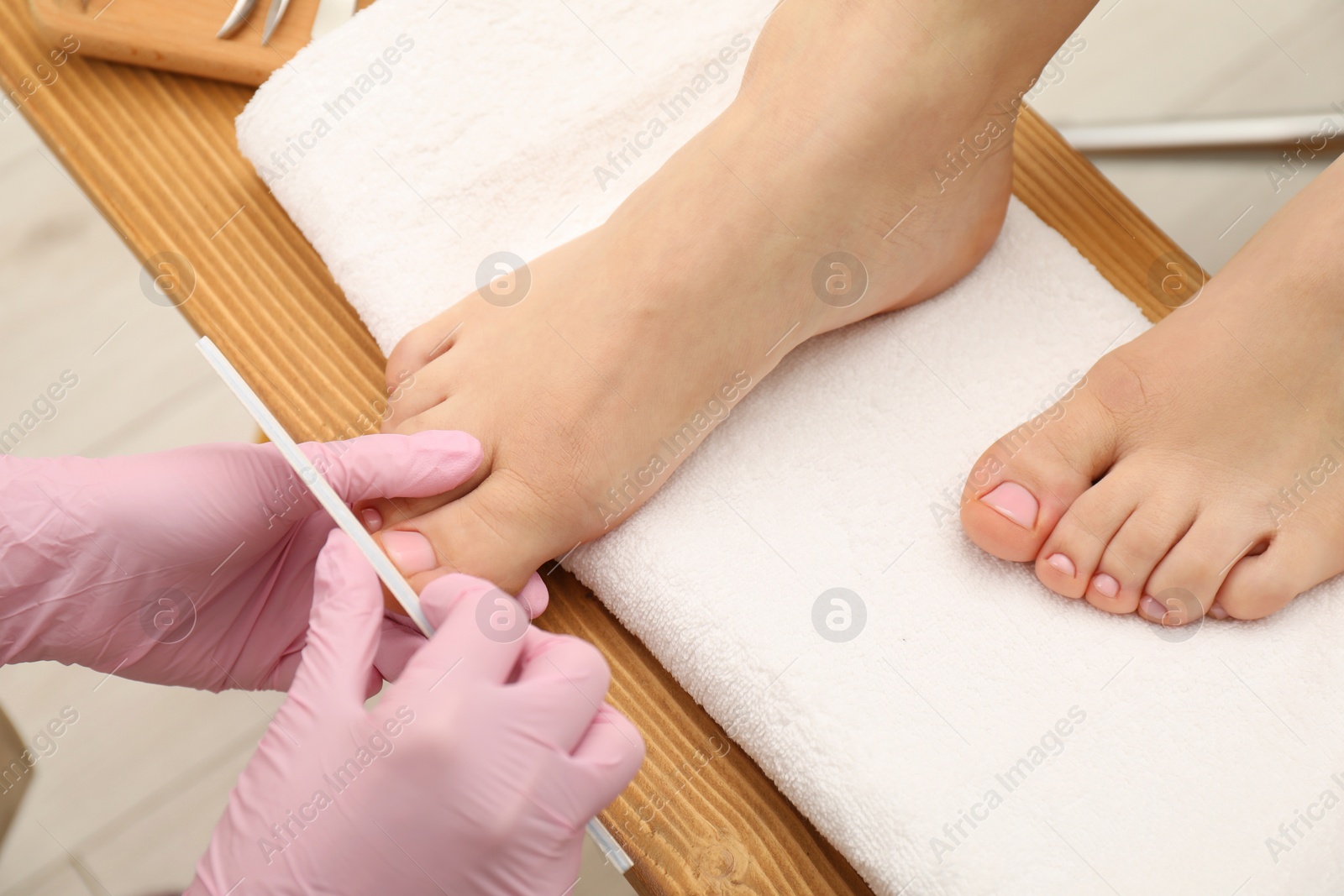 Photo of Professional pedicurist filing client`s toenails in beauty salon, closeup