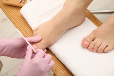 Professional pedicurist filing client`s toenails in beauty salon, closeup