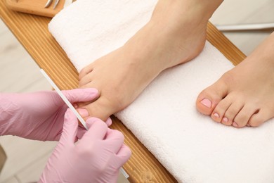 Photo of Professional pedicurist filing client`s toenails in beauty salon, closeup