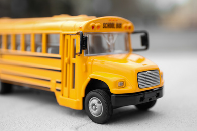 Photo of Yellow toy school bus against blurred background, closeup. Transport for students