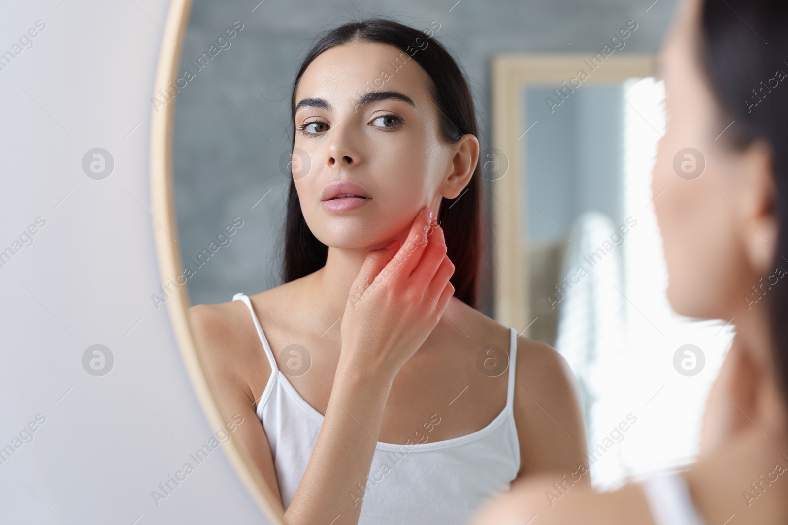 Photo of Suffering from allergy. Young woman looking at her irritated skin near mirror indoors