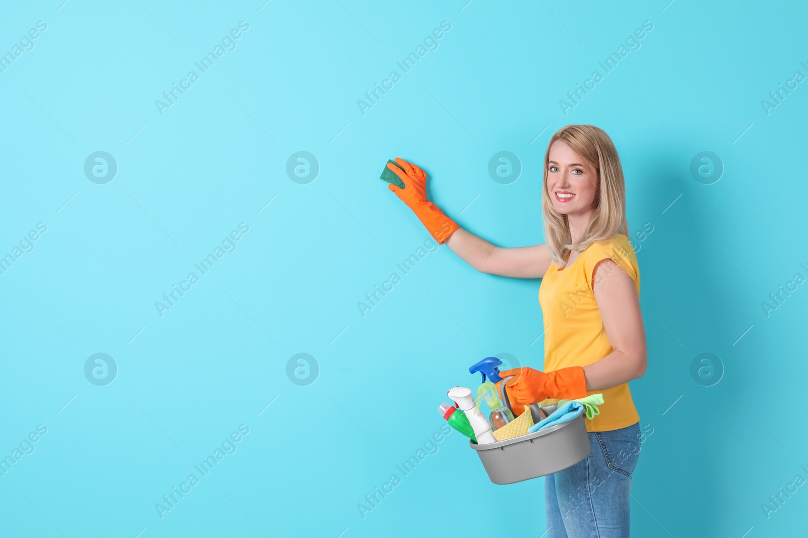 Photo of Woman in gloves cleaning color wall with sponge