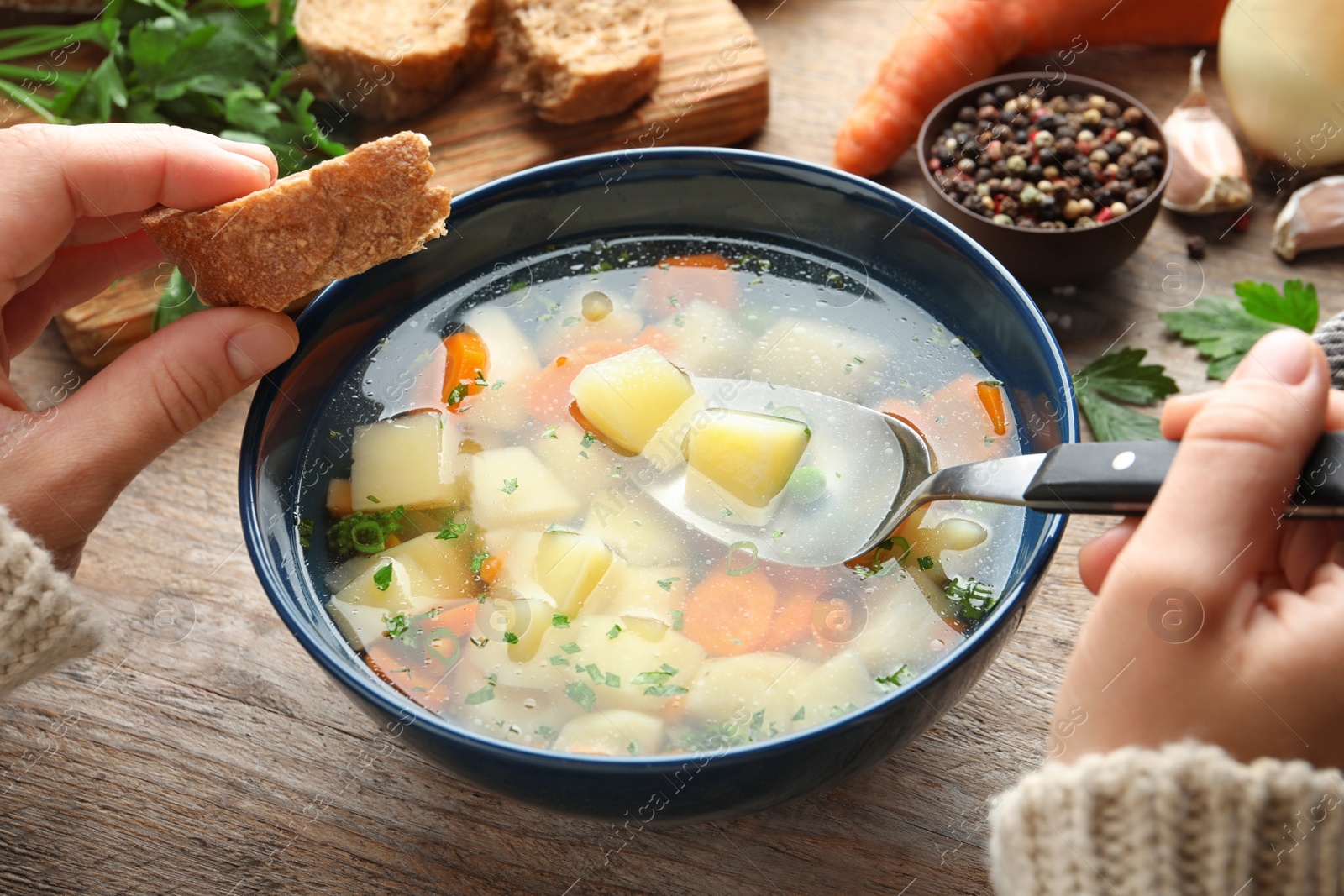 Photo of Woman eating fresh homemade vegetable soup at wooden table, closeup