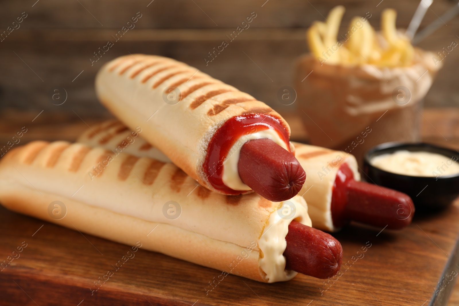 Photo of Delicious french hot dogs, fries and dip sauce on wooden board, closeup