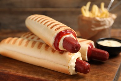 Photo of Delicious french hot dogs, fries and dip sauce on wooden board, closeup
