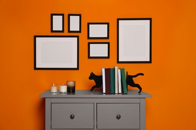 Photo of Empty frames hanging on orange wall in room above chest of drawers with decorative elements. Mockup for design