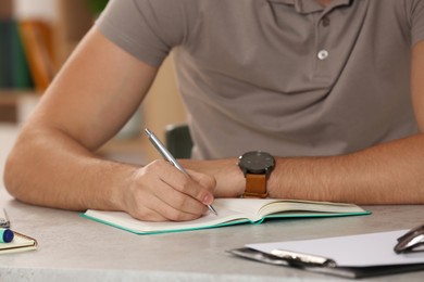 Man writing in notebook at table indoors, closeup