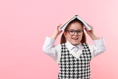 Photo of Cute little girl in glasses with open book on pink background. Space for text