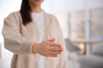 Photo of Young woman offering handshake indoors, closeup. Space for text
