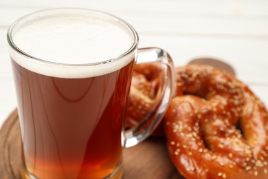 Mug of beer with tasty freshly baked pretzels on white table, closeup