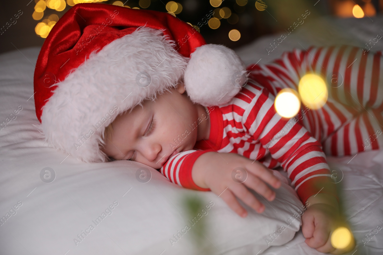 Photo of Baby in Christmas pajamas and Santa hat sleeping on bed indoors