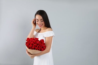 Photo of Happy woman with red tulip bouquet on light grey background, space for text. 8th of March celebration