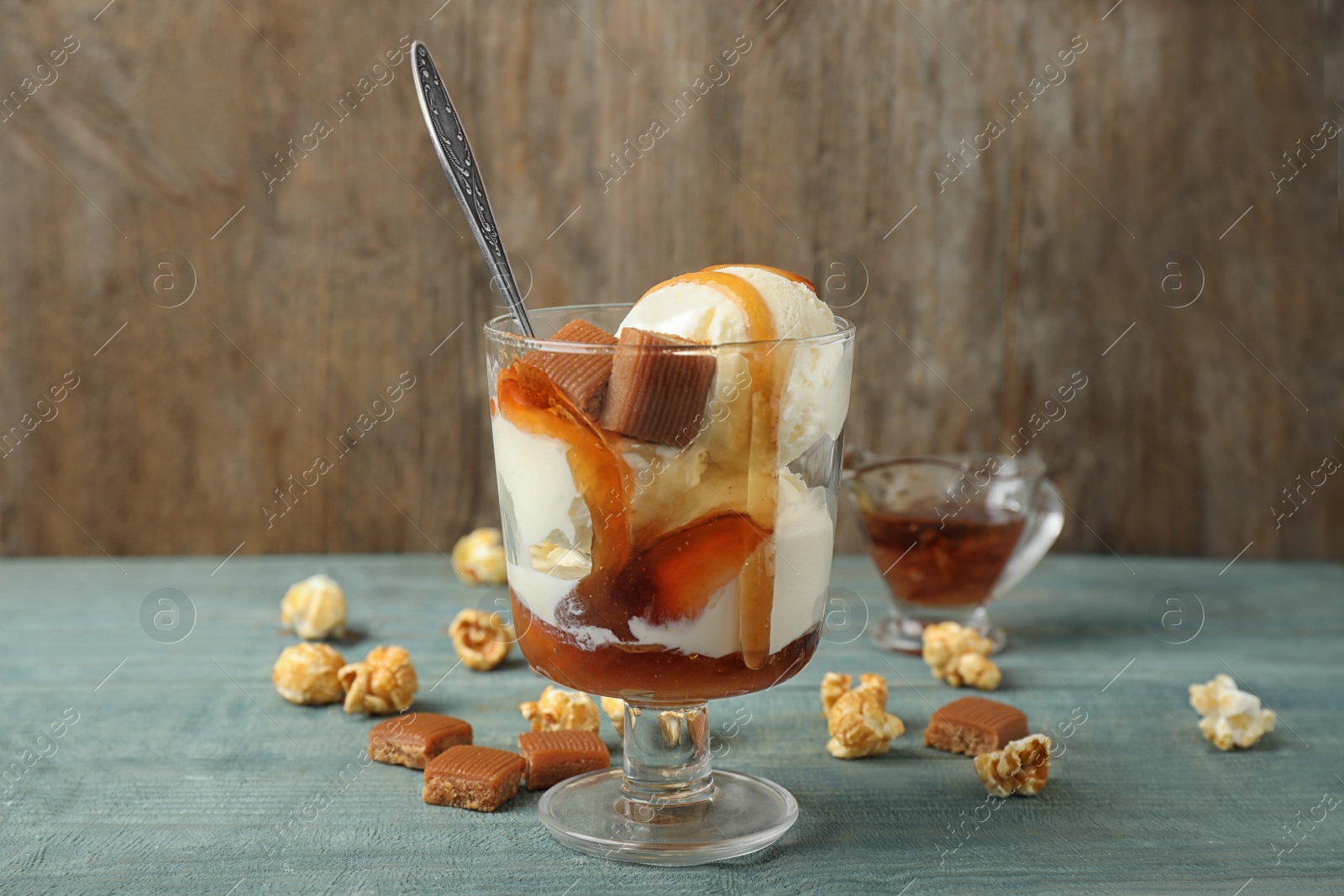 Photo of Delicious ice cream with caramel topping in dessert bowl on blue wooden table