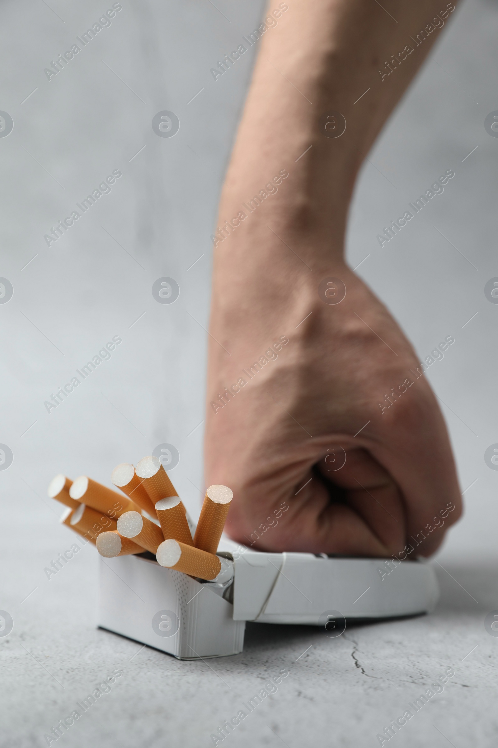 Photo of Stop smoking. Man crushing pack with cigarettes on light background, closeup