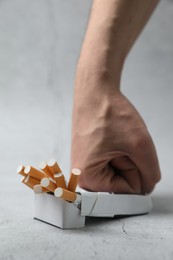 Photo of Stop smoking. Man crushing pack with cigarettes on light background, closeup