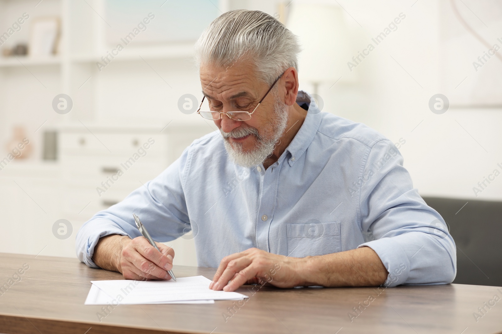 Photo of Senior man signing Last Will and Testament at wooden table indoors