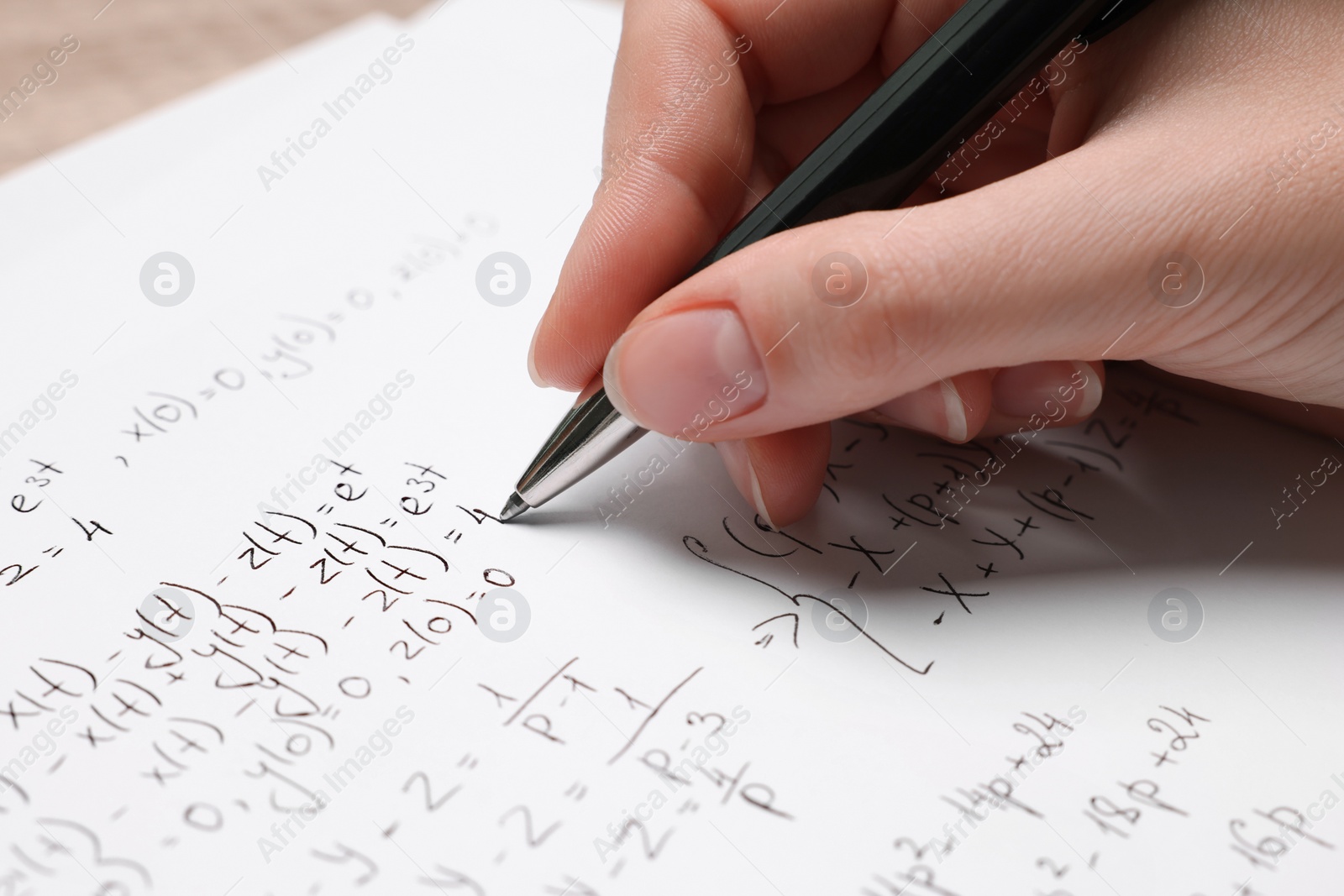 Photo of Student writing different mathematical formulas on paper, closeup